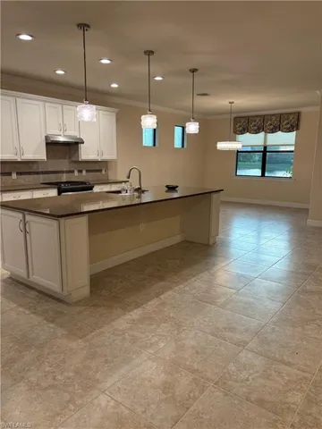 Kitchen featuring light tile patterned flooring, sink, decorative backsplash, crown molding, and a center island with sink