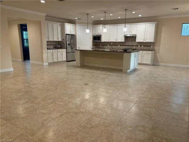 Kitchen with stainless steel appliances, decorative backsplash, sink, a center island with sink, and white cabinets