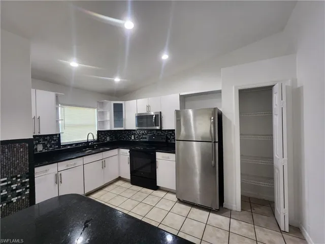 Kitchen with lofted ceiling, open shelves, stainless steel appliances, white cabinets, and light tile patterned flooring