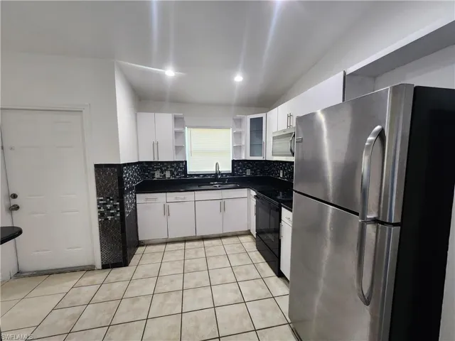 Kitchen with stainless steel appliances, dark countertops, open shelves, white cabinets, and light tile patterned flooring