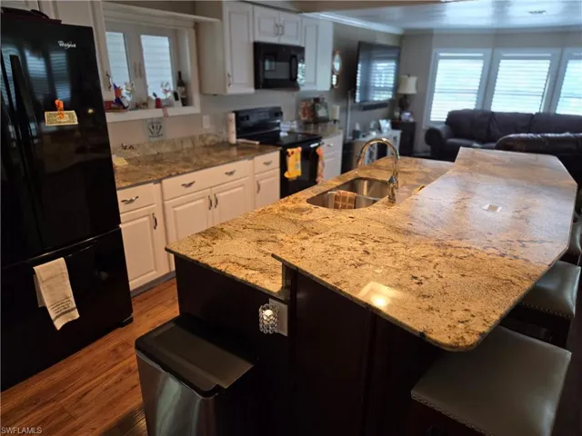 Kitchen with black appliances, white cabinetry, hardwood / wood-style floors, and sink