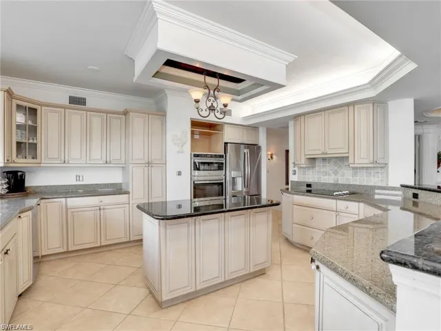 Kitchen featuring cream cabinets, a raised ceiling, ornamental molding, dark stone counters, and stainless steel appliances