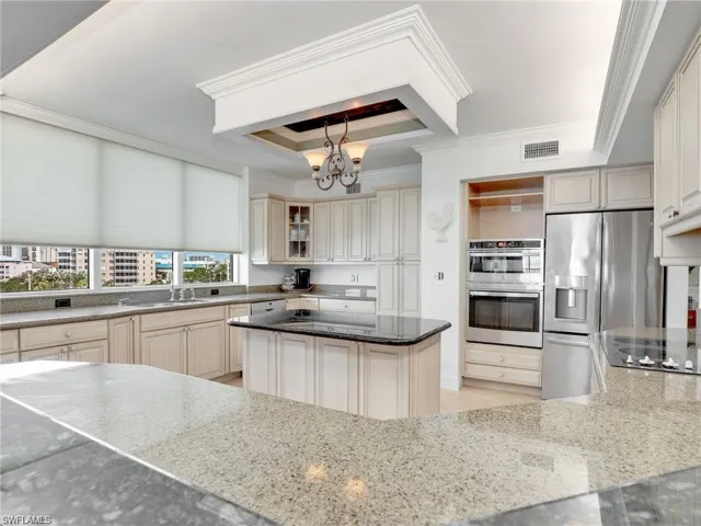 Kitchen featuring appliances with stainless steel finishes, dark stone counters, pendant lighting, ornamental molding, and a raised ceiling