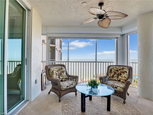 Sunroom / solarium with view of water and beach, plenty of natural light, a textured wall, and a textured ceiling