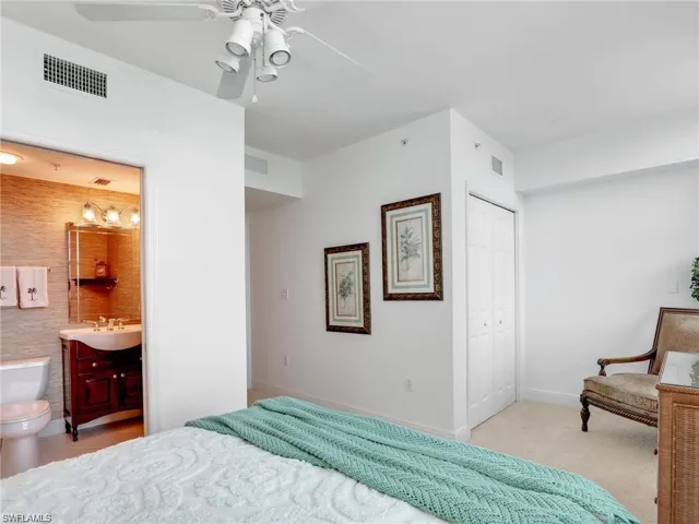 Bedroom with a closet, a ceiling fan, ensuite bathroom, and light carpet