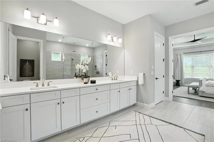 Ensuite bathroom with double vanity, tiled shower, plenty of natural light, and a ceiling fan