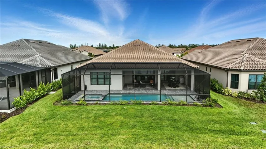 Back of property with a lawn, a tiled roof, stucco siding, a patio, and a pool with connected hot tub