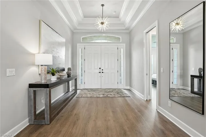 Entrance foyer with wood finished floors, a tray ceiling, a chandelier, and ornamental molding
