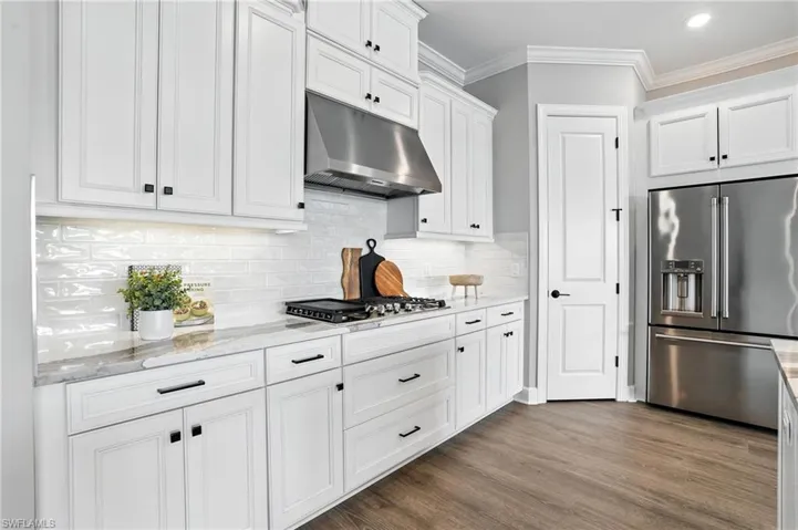 Kitchen featuring stainless steel appliances, under cabinet range hood, white cabinetry, crown molding, and backsplash