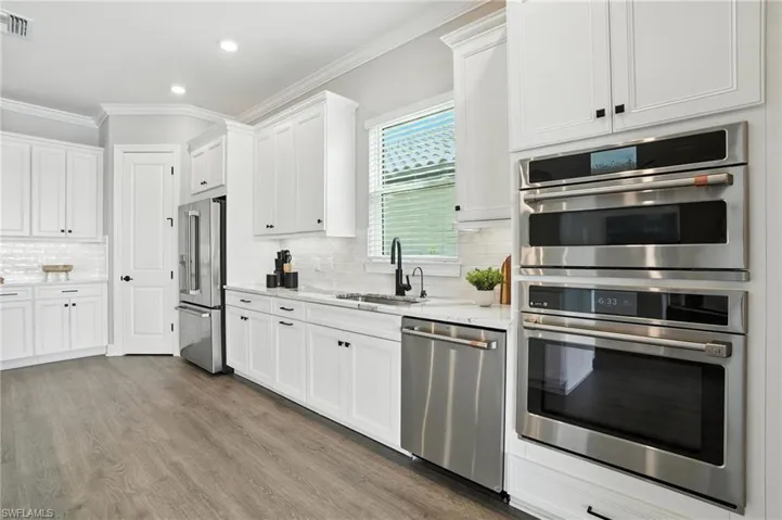Kitchen featuring appliances with stainless steel finishes, ornamental molding, white cabinetry, wood finished floors, and decorative backsplash