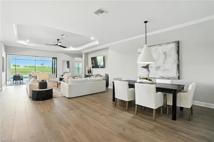 Living area with ornamental molding, a raised ceiling, wood finished floors, a ceiling fan, and recessed lighting