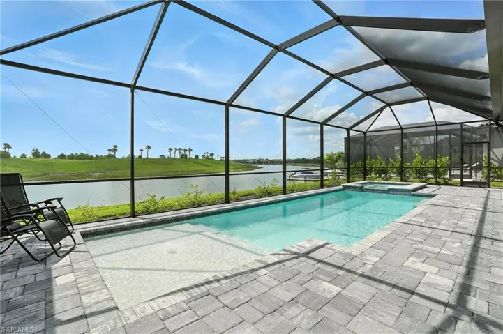View of pool with a water view, a pool with connected hot tub, a patio area, and glass enclosure