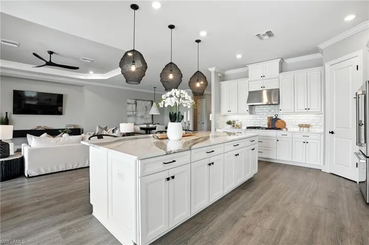 Kitchen featuring open floor plan, ornamental molding, wood finished floors, light stone countertops, and a kitchen island