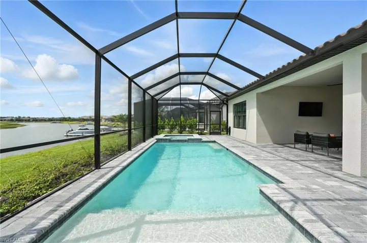 View of swimming pool with a patio area, a water view, a pool with connected hot tub, and a lanai