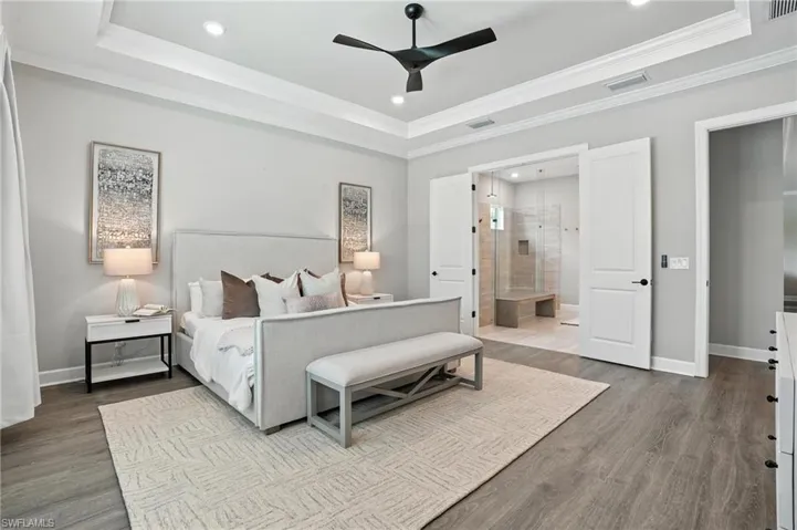 Bedroom with a tray ceiling, recessed lighting, ornamental molding, wood finished floors, and ensuite bathroom