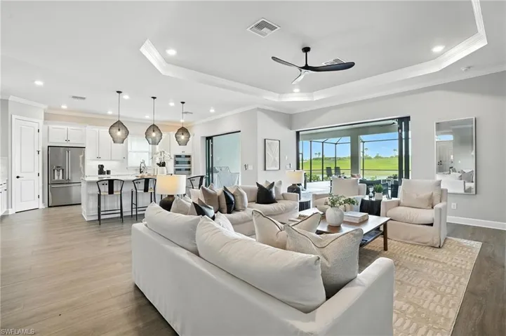 Living area featuring a tray ceiling, a ceiling fan, wood finished floors, recessed lighting, and ornamental molding