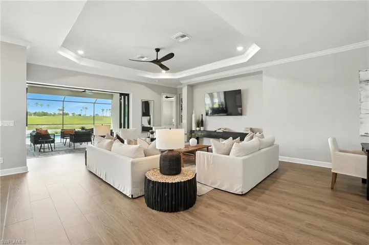 Living room featuring a raised ceiling, a ceiling fan, wood finished floors, ornamental molding, and recessed lighting