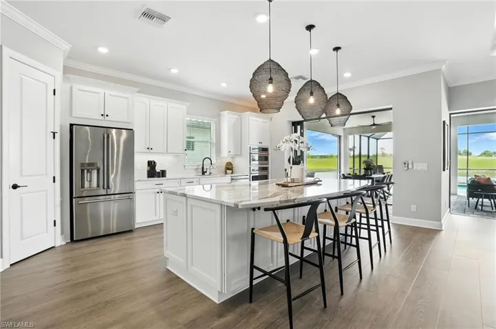 Kitchen with appliances with stainless steel finishes, a large island, wood finished floors, white cabinets, and recessed lighting