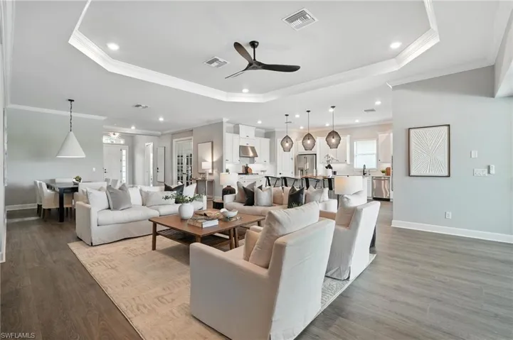 Living area featuring a raised ceiling, a ceiling fan, wood finished floors, ornamental molding, and recessed lighting