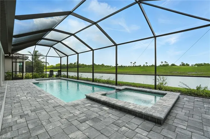 View of swimming pool featuring a patio area, a water view, a pool with connected hot tub, and a lanai