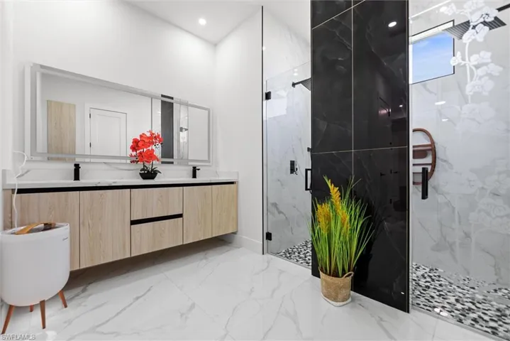 Bathroom with double vanity, a marble finish shower, light marble finish floors, and recessed lighting