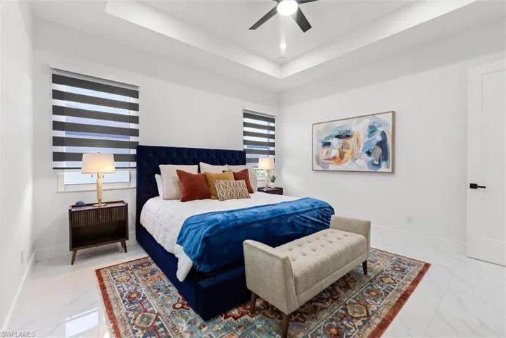 Bedroom featuring ceiling fan, light marble finish flooring, and a raised ceiling