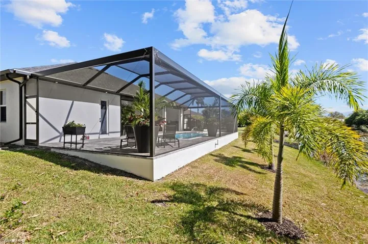 Rear view of house featuring stucco siding, a sunroom, a lawn, and a lanai