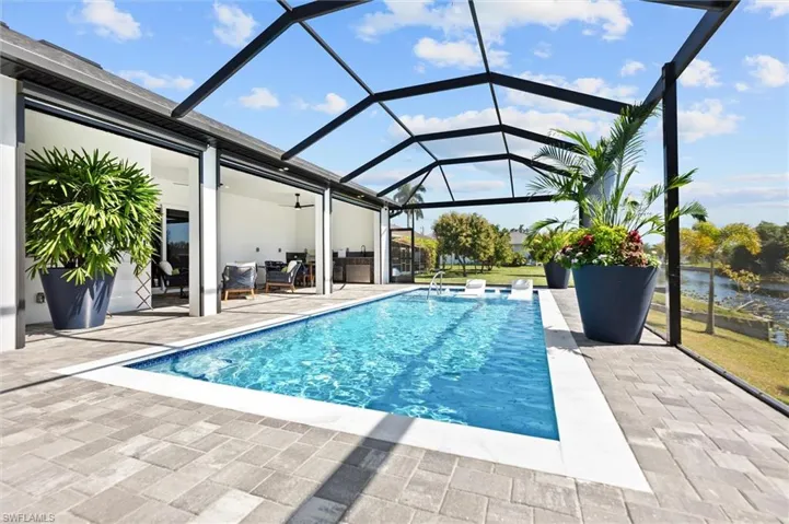 Outdoor pool featuring a sunroom, glass enclosure, a patio, and a water view