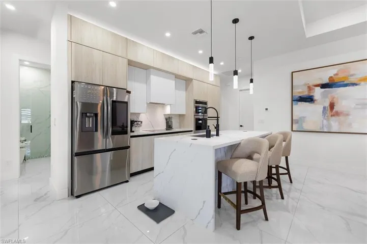 Two tone kitchen featuring stainless steel appliances, a kitchen breakfast bar, light stone counters, a kitchen island with sink, and pendant lighting