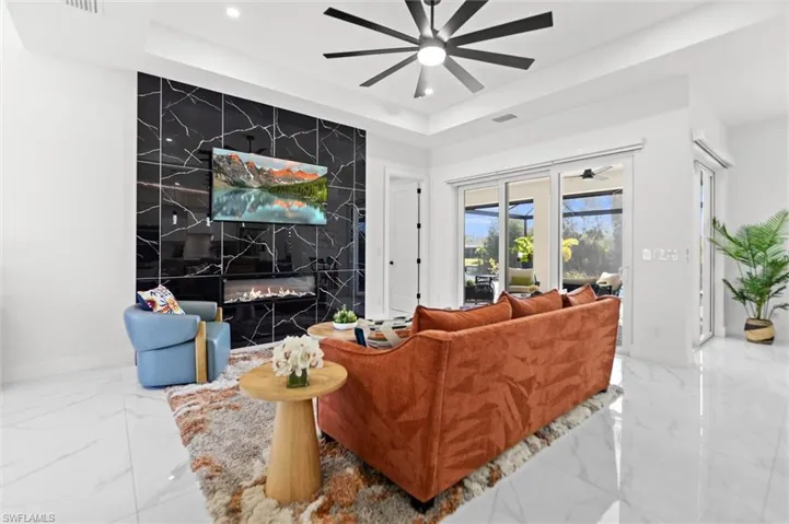 Living room featuring a tray ceiling, a ceiling fan, an accent wall, a premium fireplace, and recessed lighting