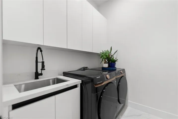 Laundry area with cabinet space, independent washer and dryer, and light marble finish floors