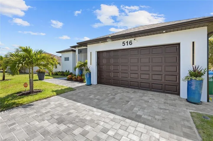 View of front of property with decorative driveway, stucco siding, a garage, and a front lawn