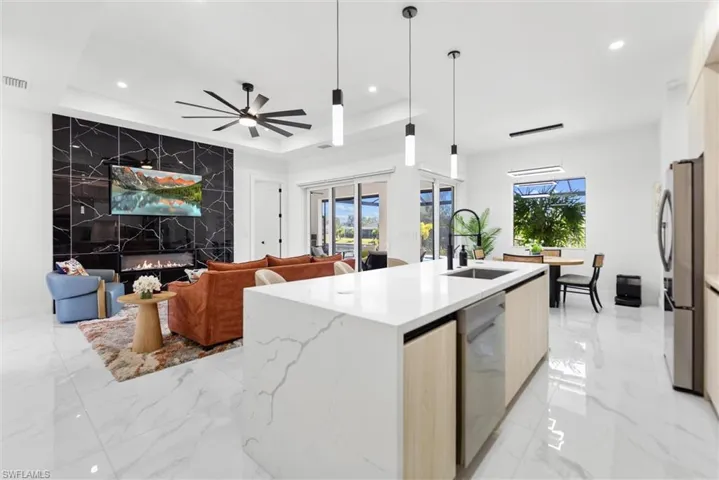 Kitchen featuring open floor plan, light wood finish cabinetry, a center island with sink, light stone counters, and decorative light fixtures