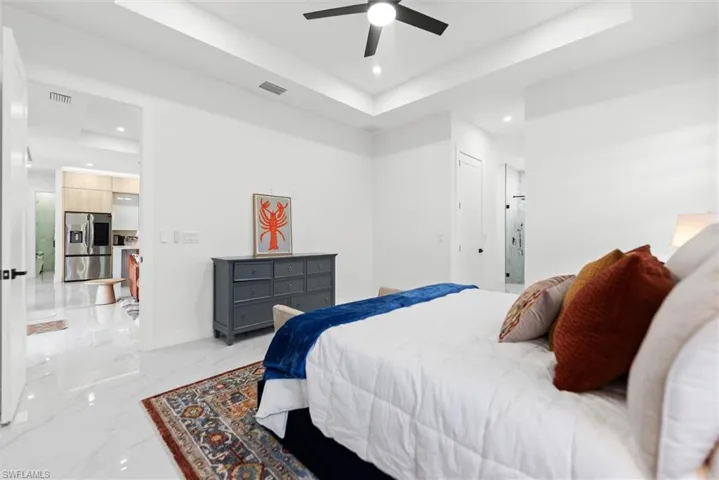 Bedroom featuring a tray ceiling, stainless steel fridge with ice dispenser, light marble finish floors, recessed lighting, and ceiling fan