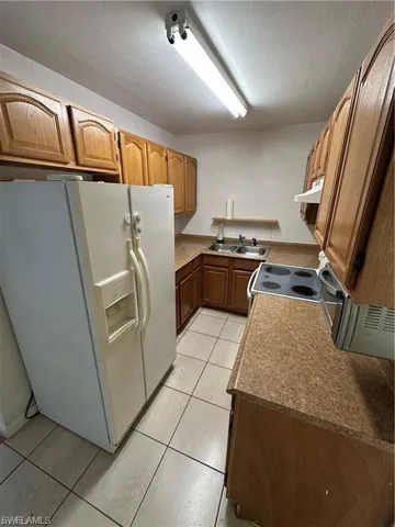 Kitchen featuring white refrigerator with ice dispenser, light tile patterned floors, and wood finish cabinetry