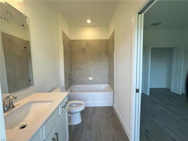 Full bathroom featuring toilet, tiled shower / bath, and vanity with extensive cabinet space