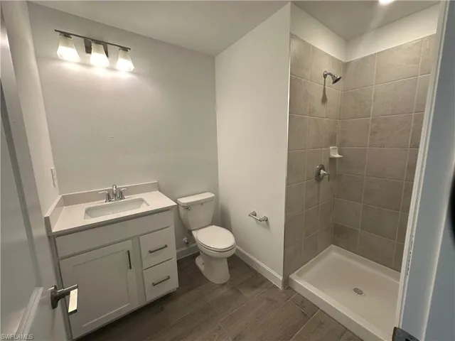 Bathroom with a tile shower, vanity, toilet, and wood-type flooring