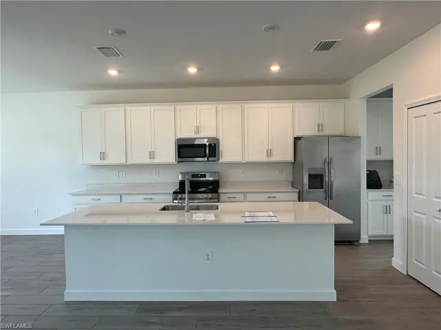 Kitchen with dark hardwood / wood-style flooring, appliances with stainless steel finishes, an island with sink, white cabinets, and sink