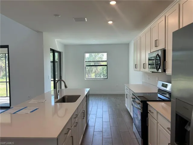Kitchen with appliances with stainless steel finishes, white cabinetry, sink, and an island with sink