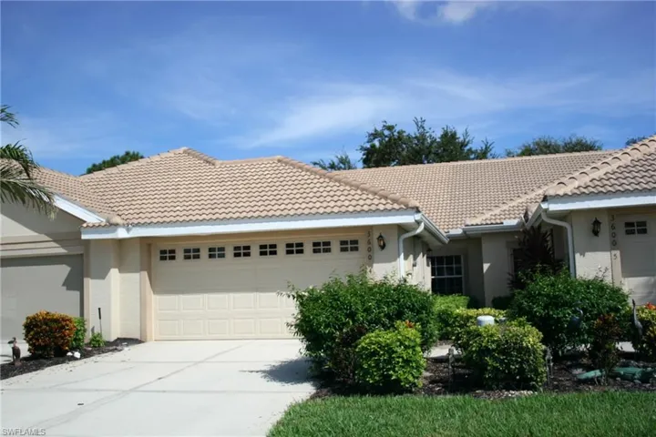 Stucco exterior with a tile roof, a two-car garage with window inserts, and mature landscaping