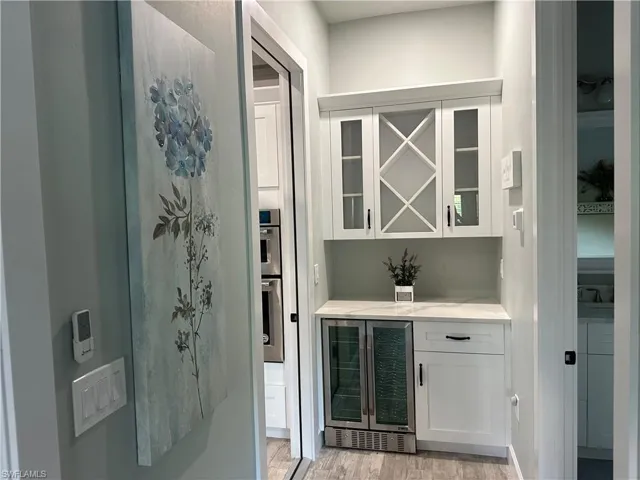 Bar featuring white cabinets, wine cooler, double oven, and light hardwood / wood-style floors