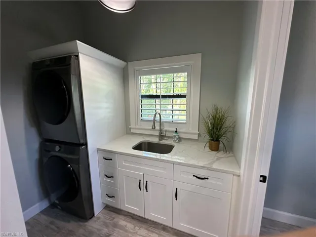 Laundry room featuring cabinets, wood-type flooring, stacked washer and dryer, and sink