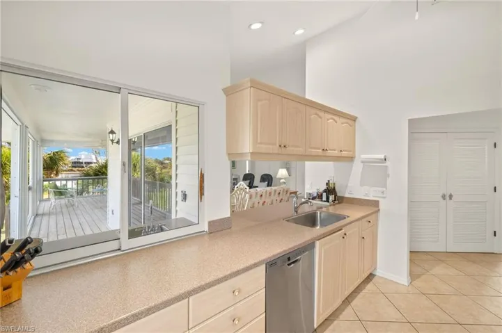 Kitchen featuring stainless steel dishwasher, light brown cabinets, light countertops, a sink, and a towering ceiling