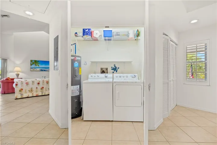 Laundry area with light tile patterned floors, water heater, washer and clothes dryer, baseboards, and recessed lighting