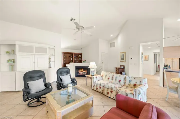 Living room with a warm lit fireplace, light tile patterned floors, a ceiling fan, high vaulted ceiling, and recessed lighting