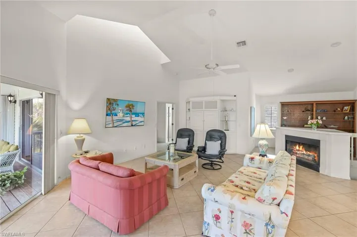 Tiled living room featuring high vaulted ceiling, healthy amount of natural light, a warm lit fireplace, and a ceiling fan