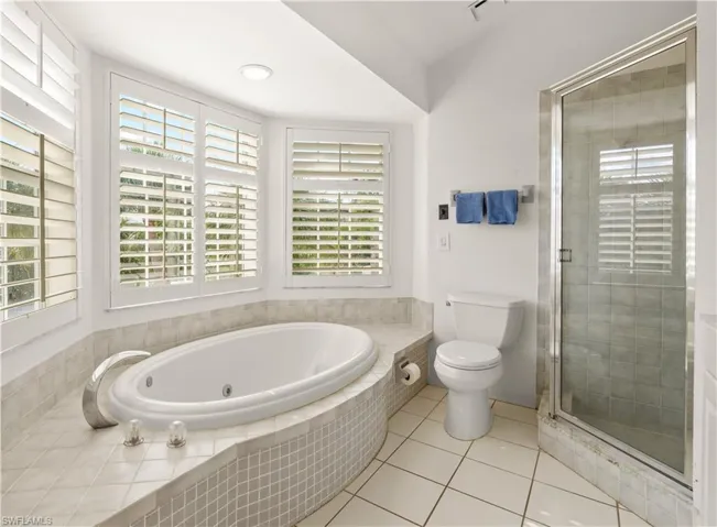 Bathroom featuring a tub with jets, toilet, a shower stall, and tile patterned floors