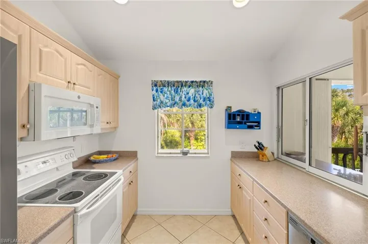 Kitchen featuring white appliances, light brown cabinets, light countertops, light tile patterned floors, and vaulted ceiling
