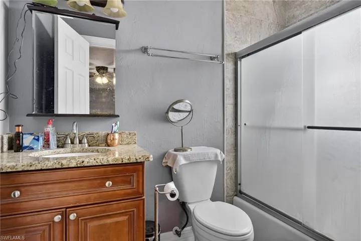 Bathroom with a textured wall, vanity, and enclosed tub / shower combo