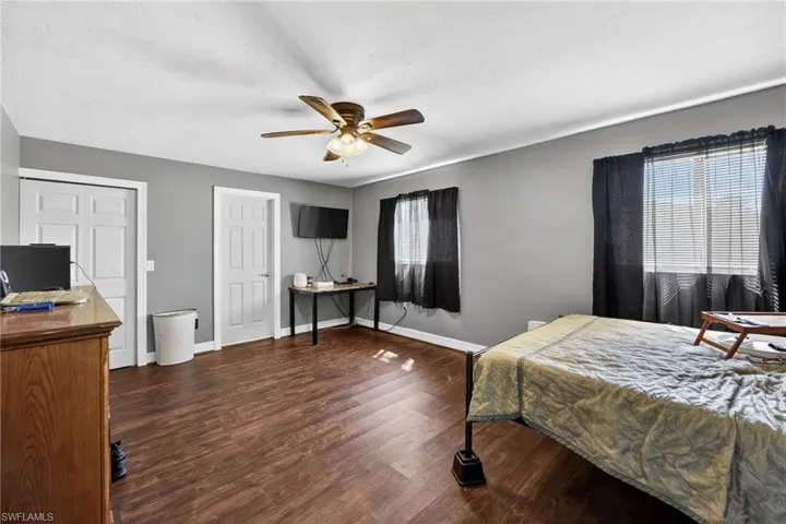 Bedroom with dark wood-style flooring, a ceiling fan, multiple closets, and an office area